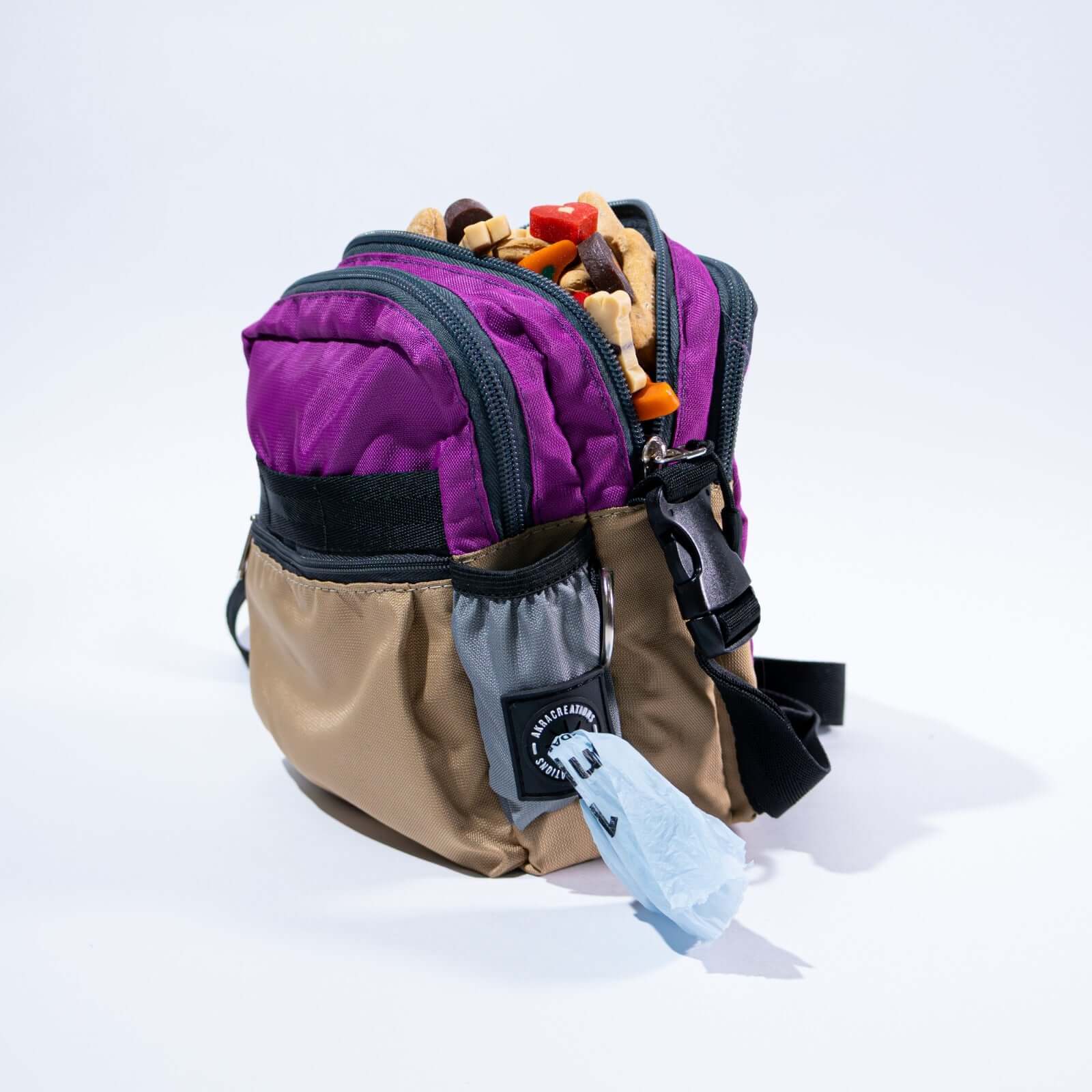 Multicolored lilac and beige crossbody dog treat bag with snacks on a white background