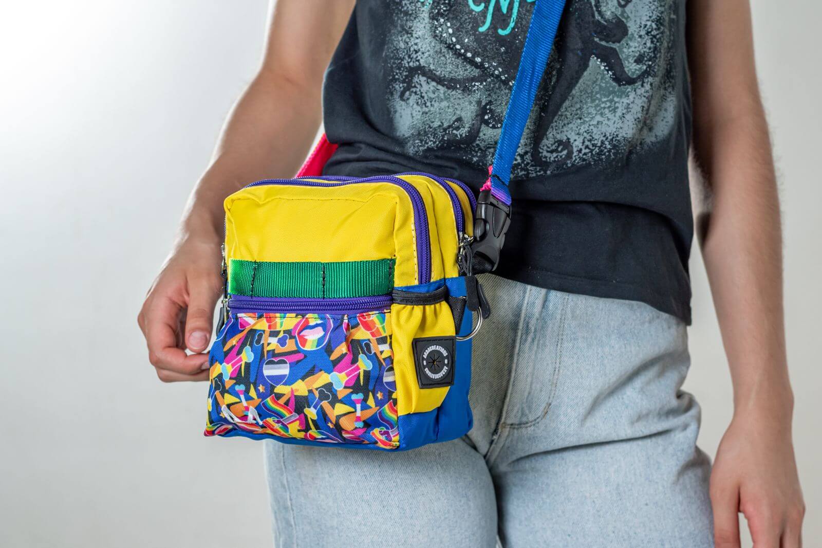 Multicolored pride/rainbow patterned crossbody dog training pouch held by a person against a neutral background