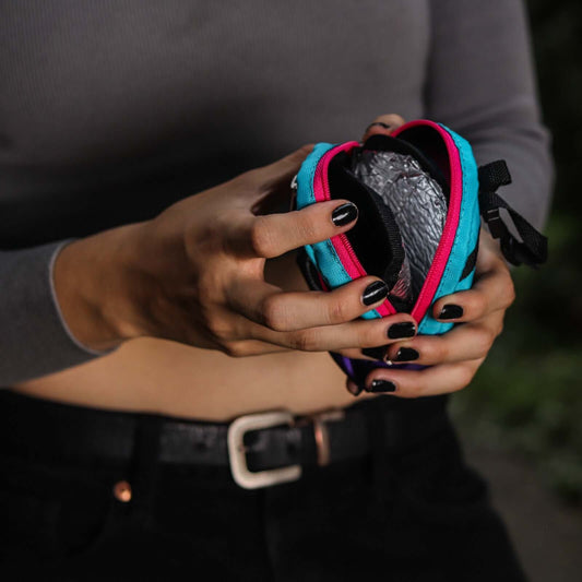 Person holding a colorful poop bag holder showing the insulated sleeve for treats with a dark background