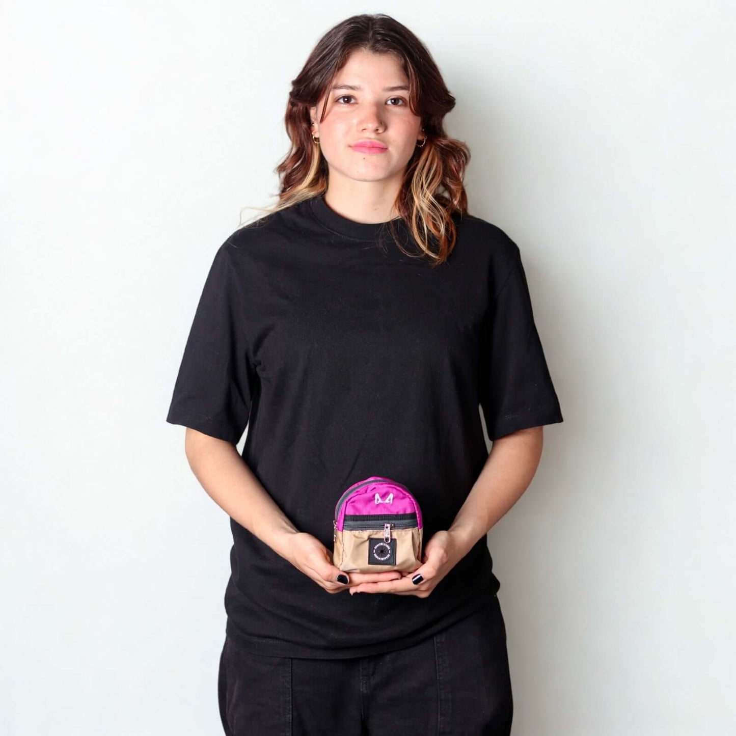 Female model holding a lilac and beige poop bag and treat bag against a plain background