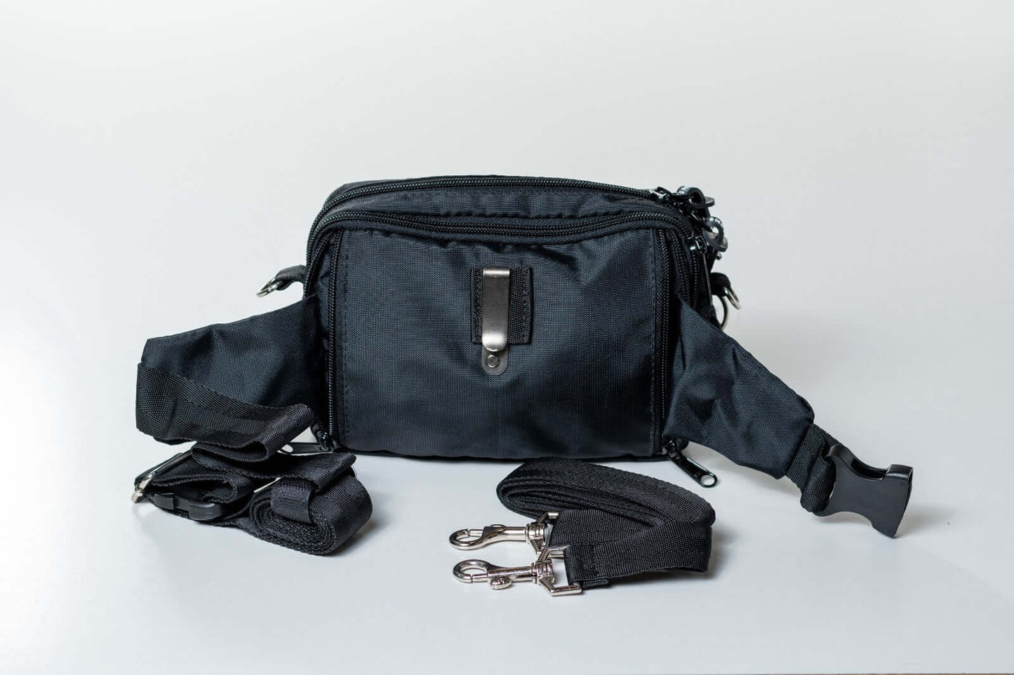 A black dog training fanny pack with multiple compartments and adjustable straps laid out on a white background.