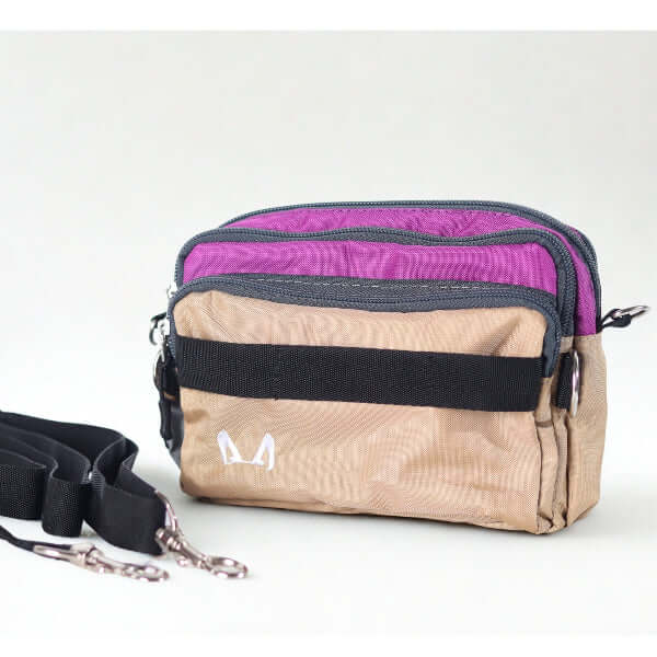 Beige crossbody bag with purple top section and black strap on a white background