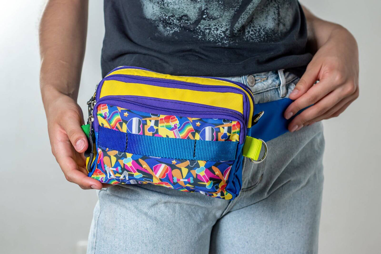 Person holding a pride/rainbow fanny pack with a plain background