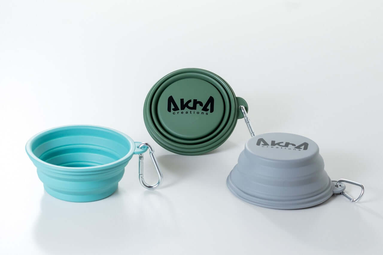 Three collapsible bowls in teal, green, and gray with 'AKUA' branding on a white background.