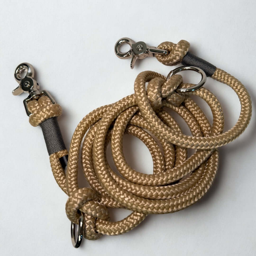 Beige rope dog leash with gray accents with metal clips on a white background
