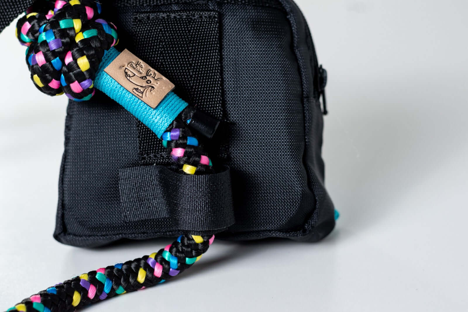 Black dog poop holder and treat bag strapped to a colorful leash on a white background
