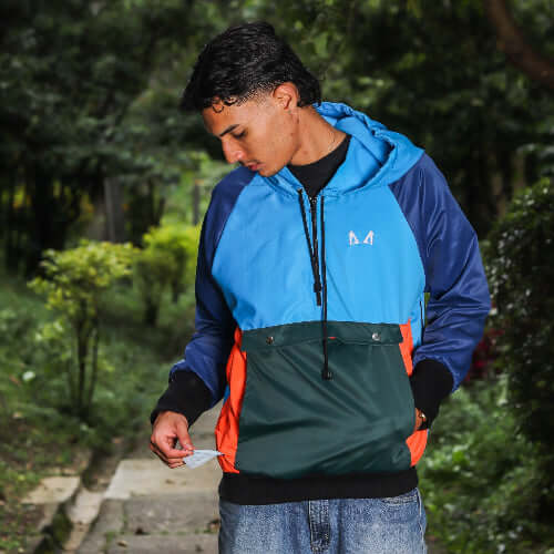 Person wearing a blue, orange, and green dog training windbreaker outdoors showing the poop bag holder compartment