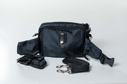 A black dog training fanny pack with multiple compartments and adjustable straps laid out on a white background.