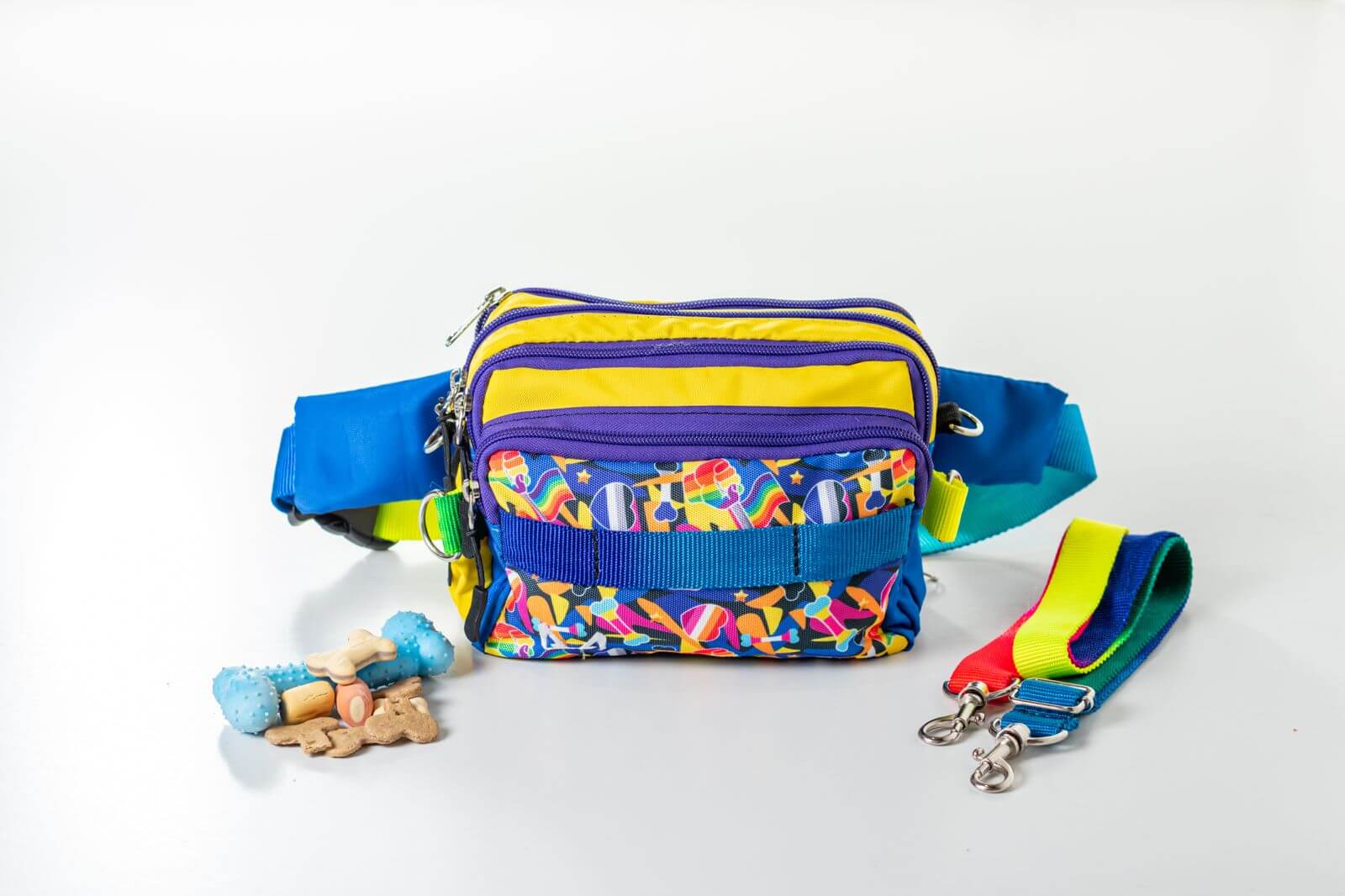 Colorful pride/rainbow waist bag with patterned strap and dog toys on a white background