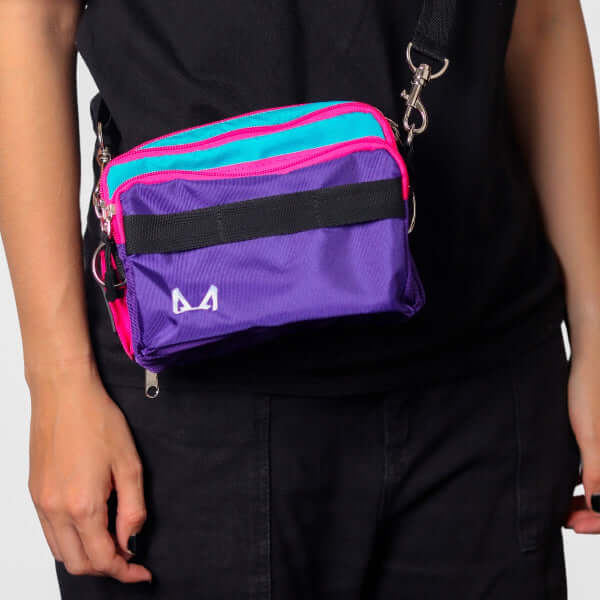 Purple crossbody bag with pink and blue accents on a person wearing a black outfit.