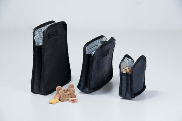 Three black removable insulated treat bags with small items on a white background