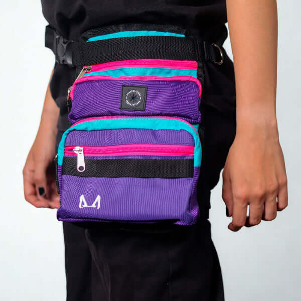 Multicolored slim fit dog thigh treat bag with purple, pink, and blue accents worn by a person on a light gray background