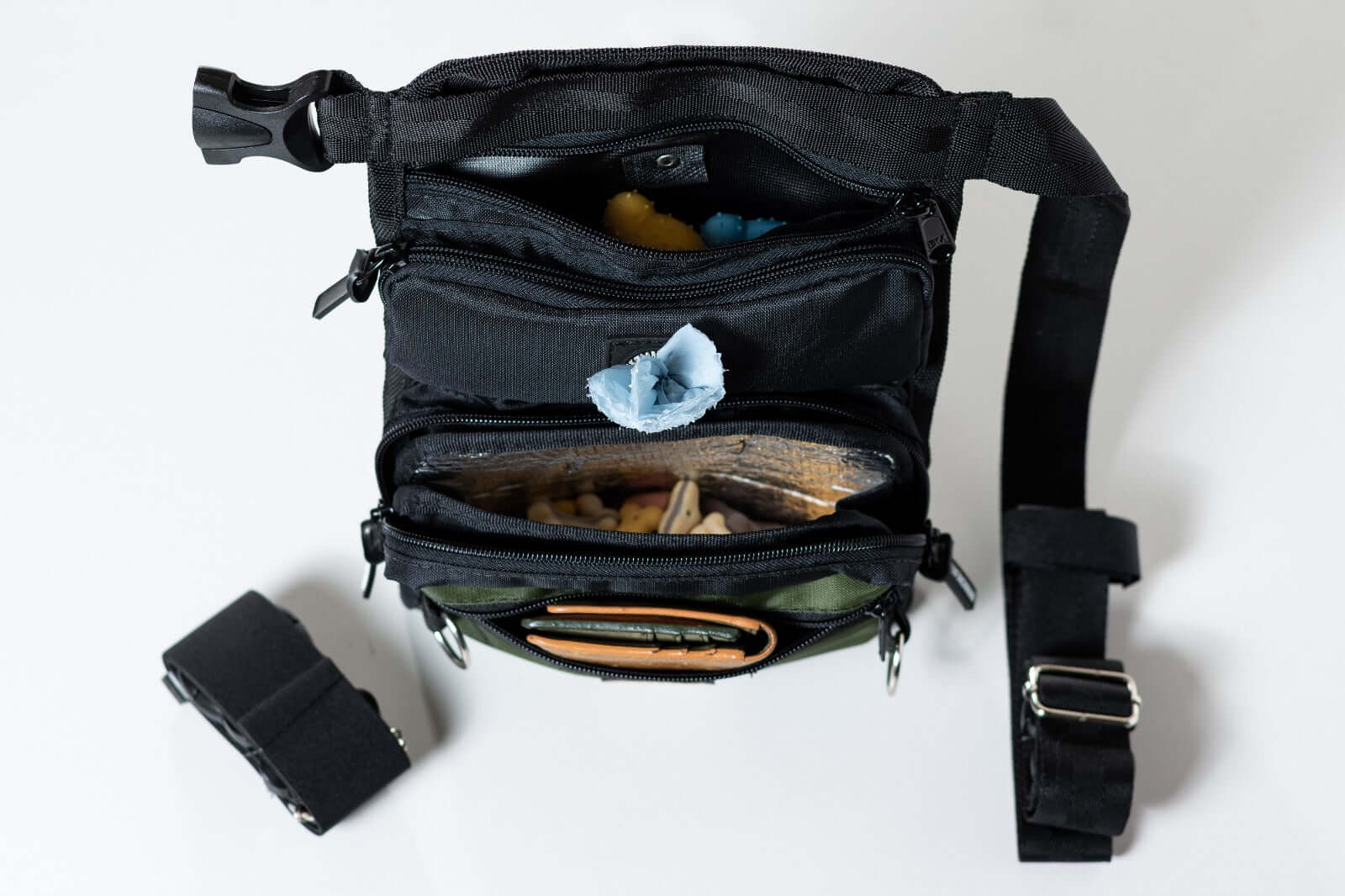 A slim fit thigh treat bag with multiple compartments, including a main pocket with an insulated sleeve, a built-in dispenser for poop bags, a small front compartment, and a back pocket. The bag is made from high-quality canvas, appears water-repellent, and has adjustable straps for comfort.