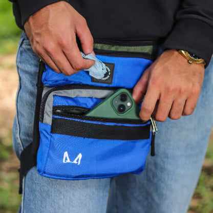 Person wearing a blue slim fit thigh treat bag with a phone and other items, outdoors.